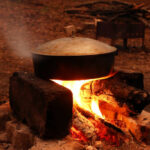 Cooking food in cast-iron pan on a bonfire near to campsite at nighttime.